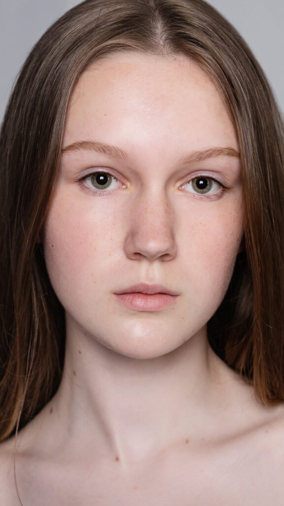 Porträt einer jungen Frau mit ungeschminktem Gesicht und glatter, natürlicher Haut, die direkt in die Kamera blickt.