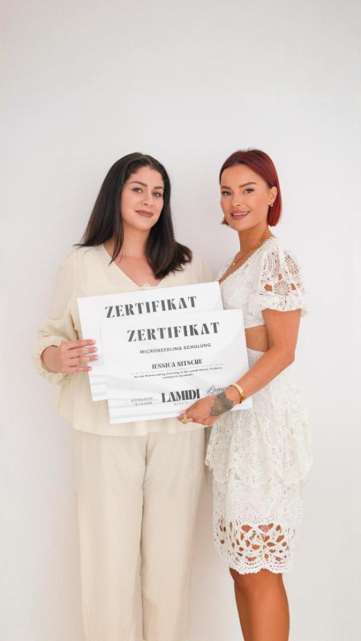 Zwei Frauen stehen vor weißem Hintergrund und halten gemeinsam ein Microneedling-Zertifikat in den Händen.